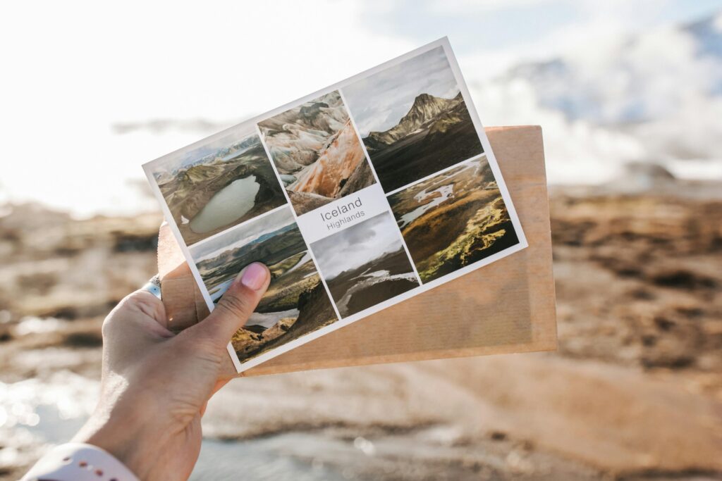 Close-up of a hand holding a scenic postcard featuring the Icelandic Highlands.